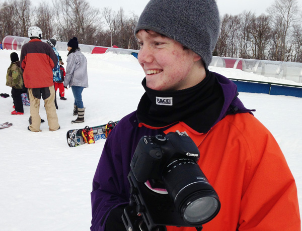 A young filmmaker smiling on a snowy ski hill